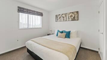 A bedroom with a large bed, a nightstand, a wall-mounted artwork, and a window with curtains.