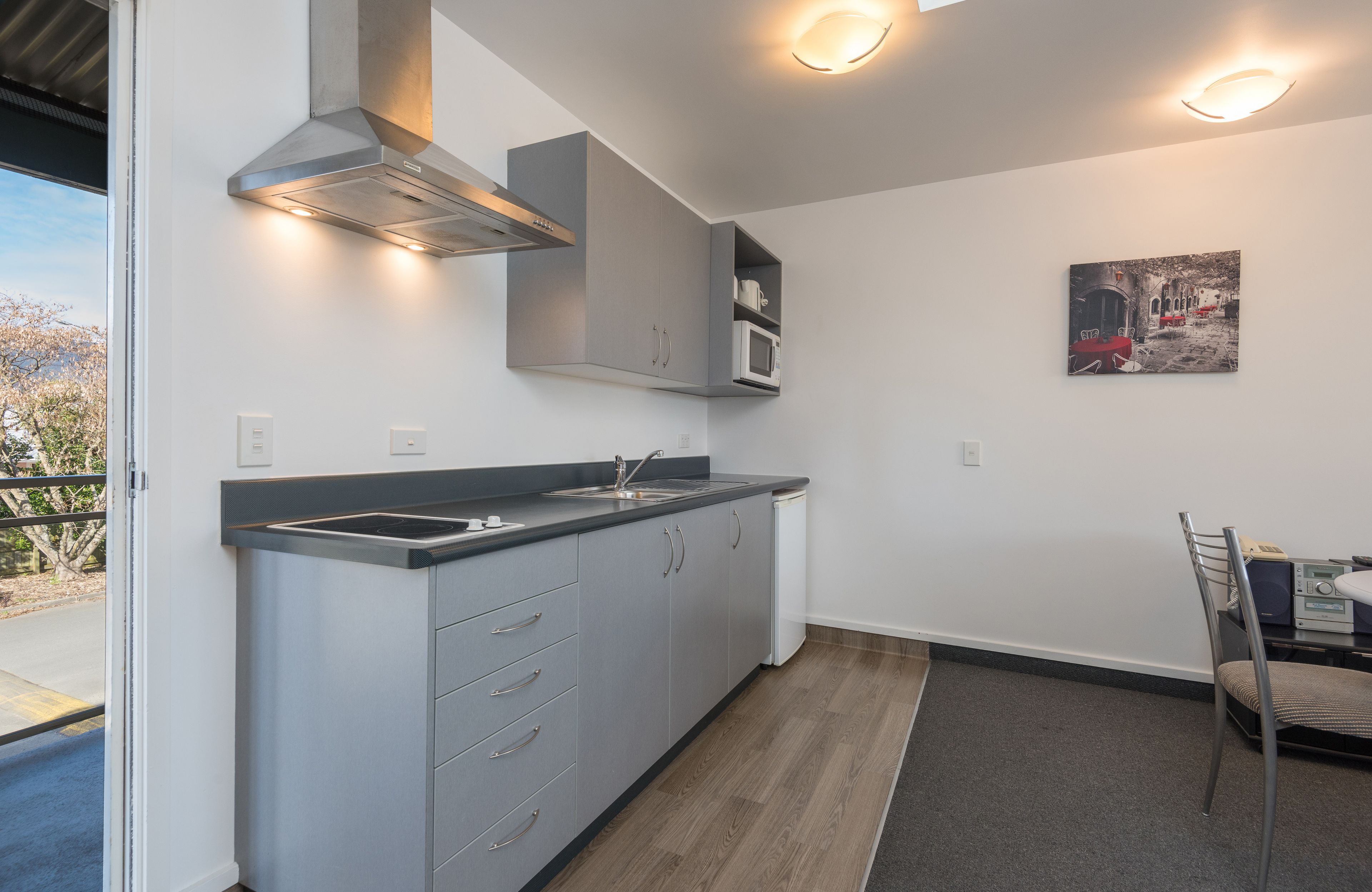 A modern kitchen with grey cabinets, a stainless steel range hood, and a microwave. There is a dining area with a table and chairs.
