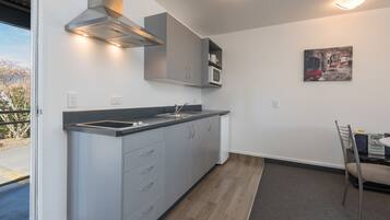A modern kitchen with grey cabinets, a stainless steel range hood, and a microwave. There is a dining area with a table and chairs.