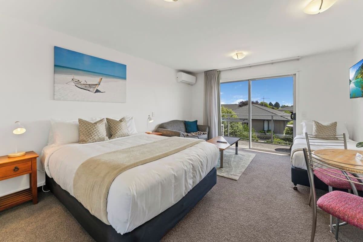 A modern hotel room with a large bed, a seating area with a table, and a balcony with a view of the landscape.