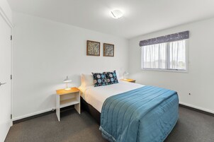 Un dormitorio con una cama, dos mesitas de noche, un velador, una ventana con cortinas y dos obras de arte en la pared.