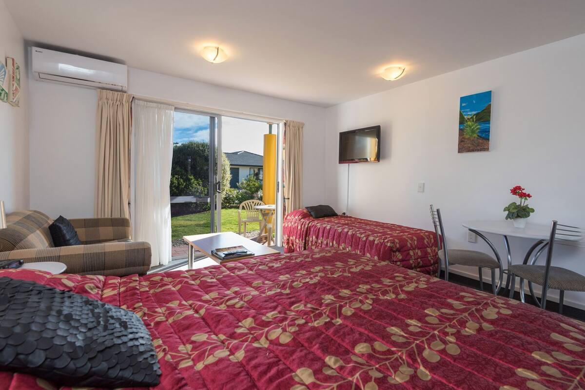 A hotel room with two beds, a TV, a dining table, and a view of the outdoors.