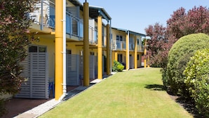 A row of yellow buildings with balconies, a well-maintained lawn, and mature trees.