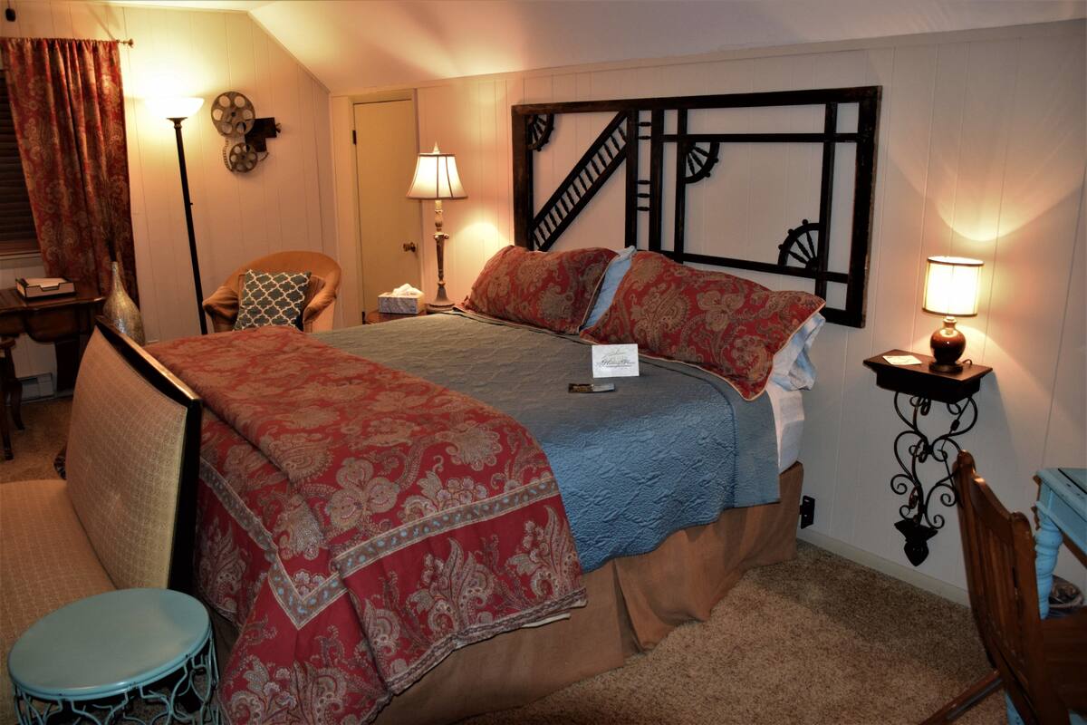 A neatly arranged bedroom with a bed, a chair, a small table, and a lamp.
