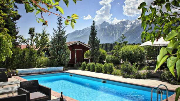Une piscine avec des chaises longues, un petit bâtiment et une montagne en arrière-plan.