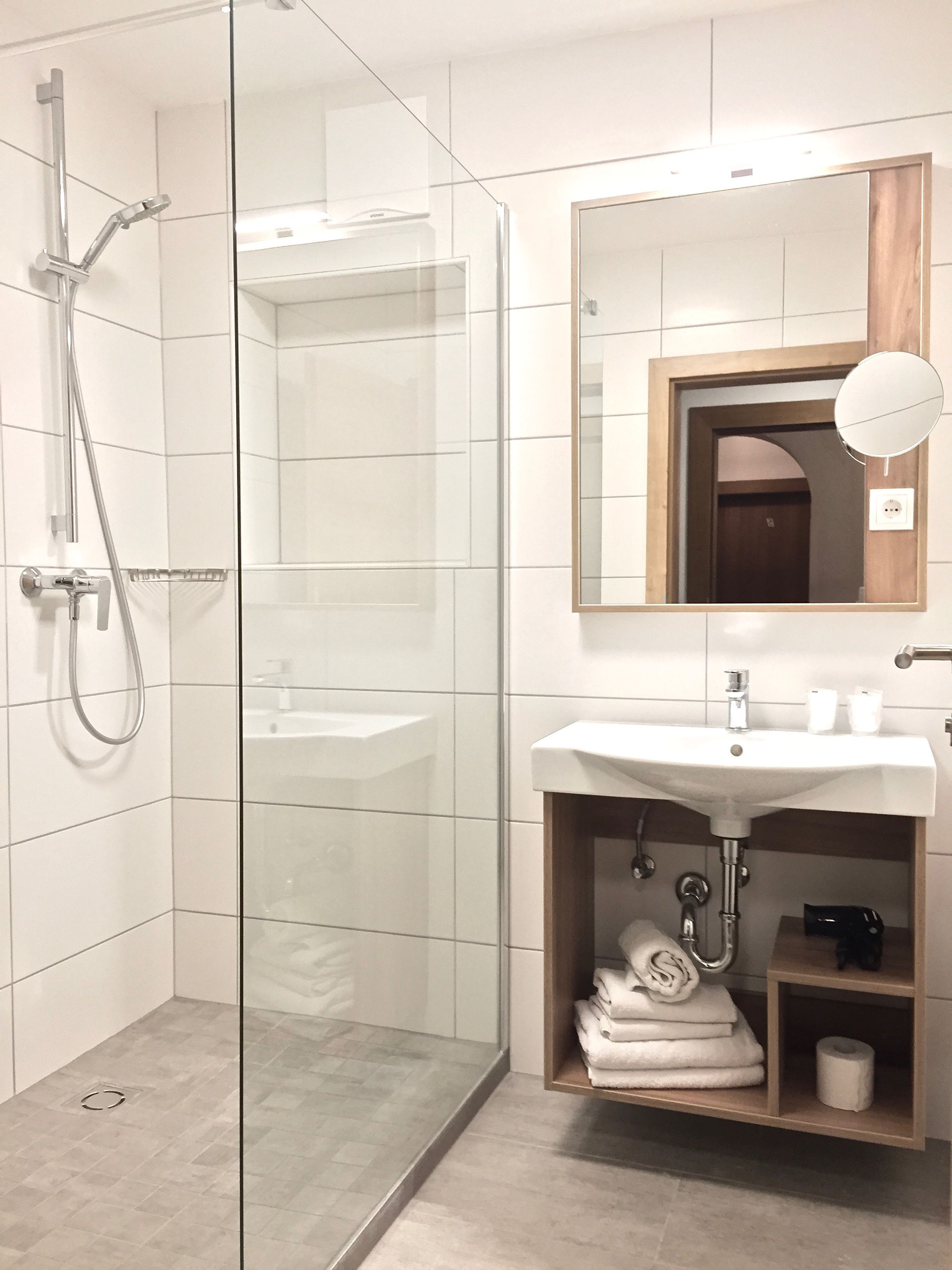 Un baño moderno con ducha de mampara de vidrio, un lavamanos blanco y un espejo encima.
