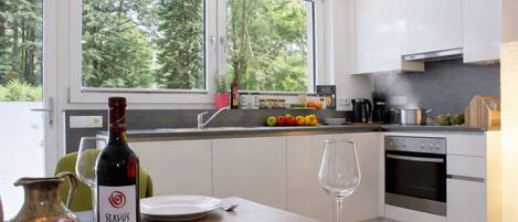 Una cocina moderna con armarios blancos, una mesa de comedor dispuesta con platos, una botella de vino y una copa.