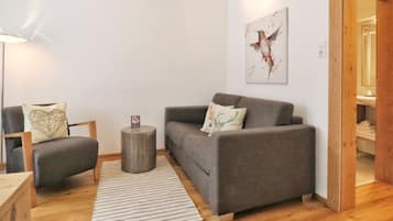 Un salon moderne avec un canapé gris, une table d’appoint en bois, un tapis à rayures et une œuvre d’art encadrée accrochée au mur.