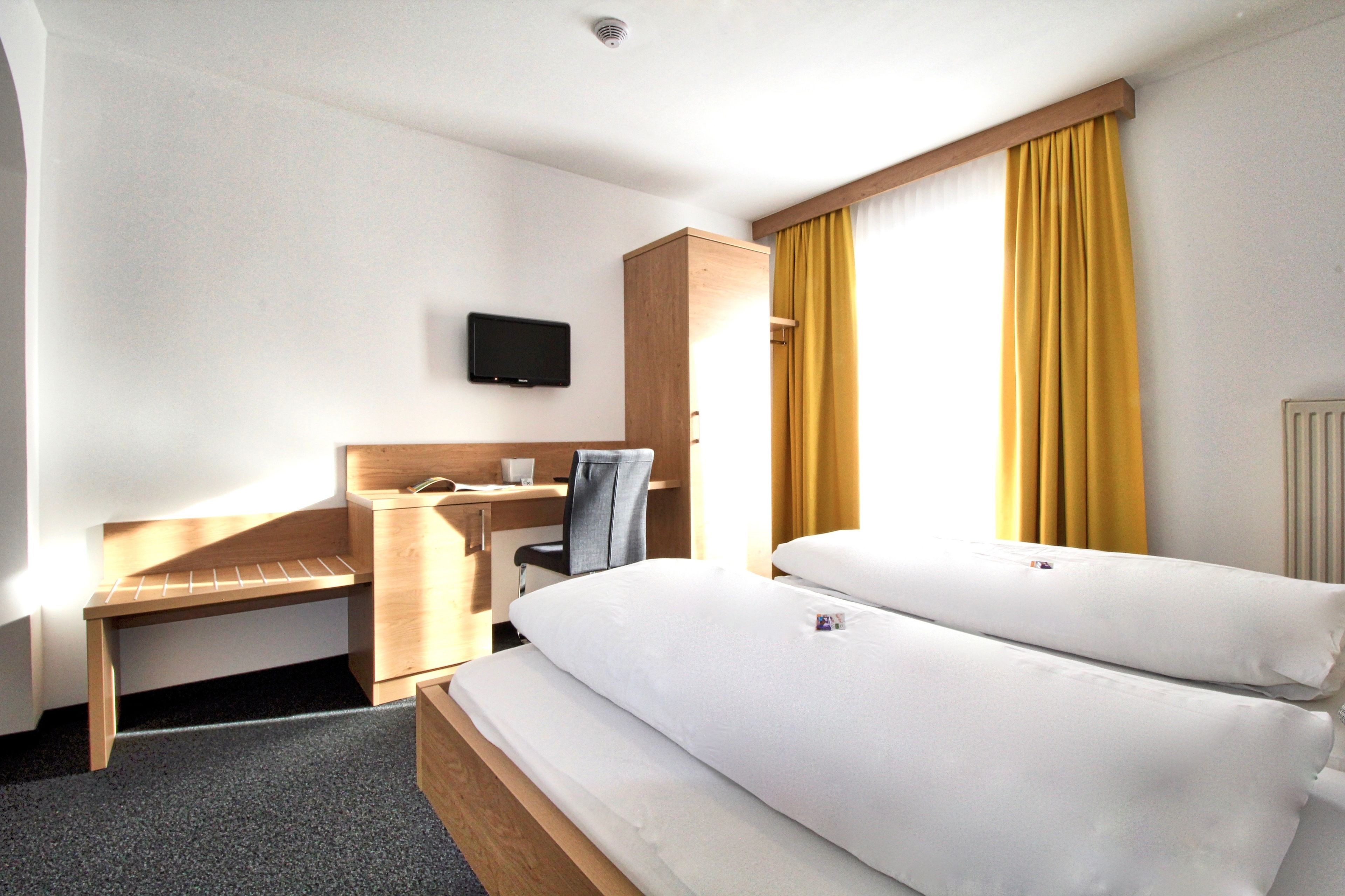 A hotel room with two beds, a desk, a chair, a television, and a wardrobe.