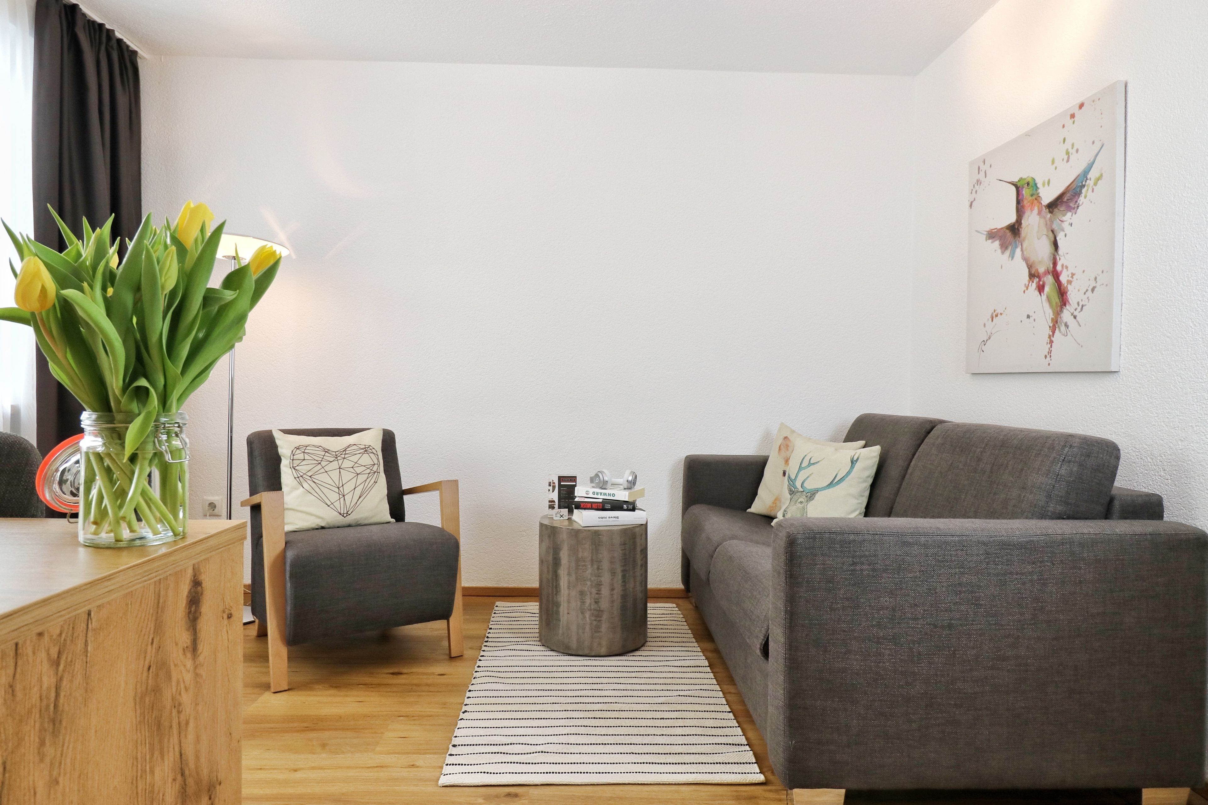Una sala de estar moderna con un sofá gris, una mesa de centro de madera y un florero con plantas verdes.