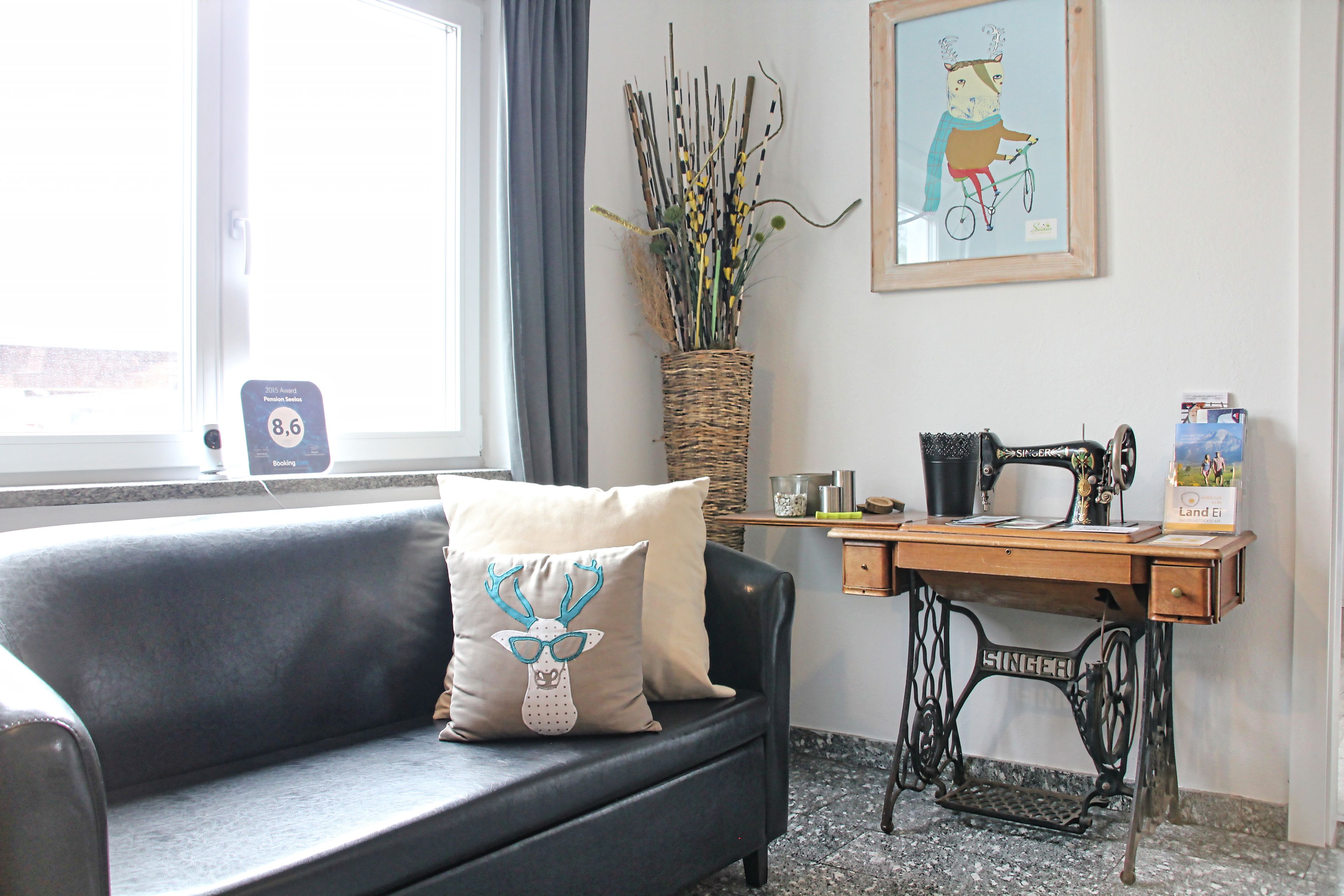 A room with a grey sofa, a vintage Singer sewing machine, a wicker basket with plants, and a framed picture on the wall.