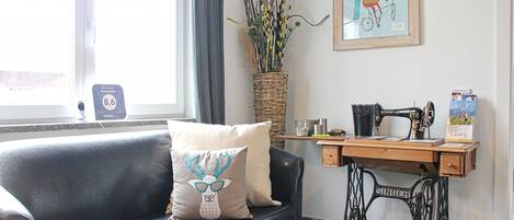 A room with a grey sofa, a vintage Singer sewing machine, a wicker basket with plants, and a framed picture on the wall.