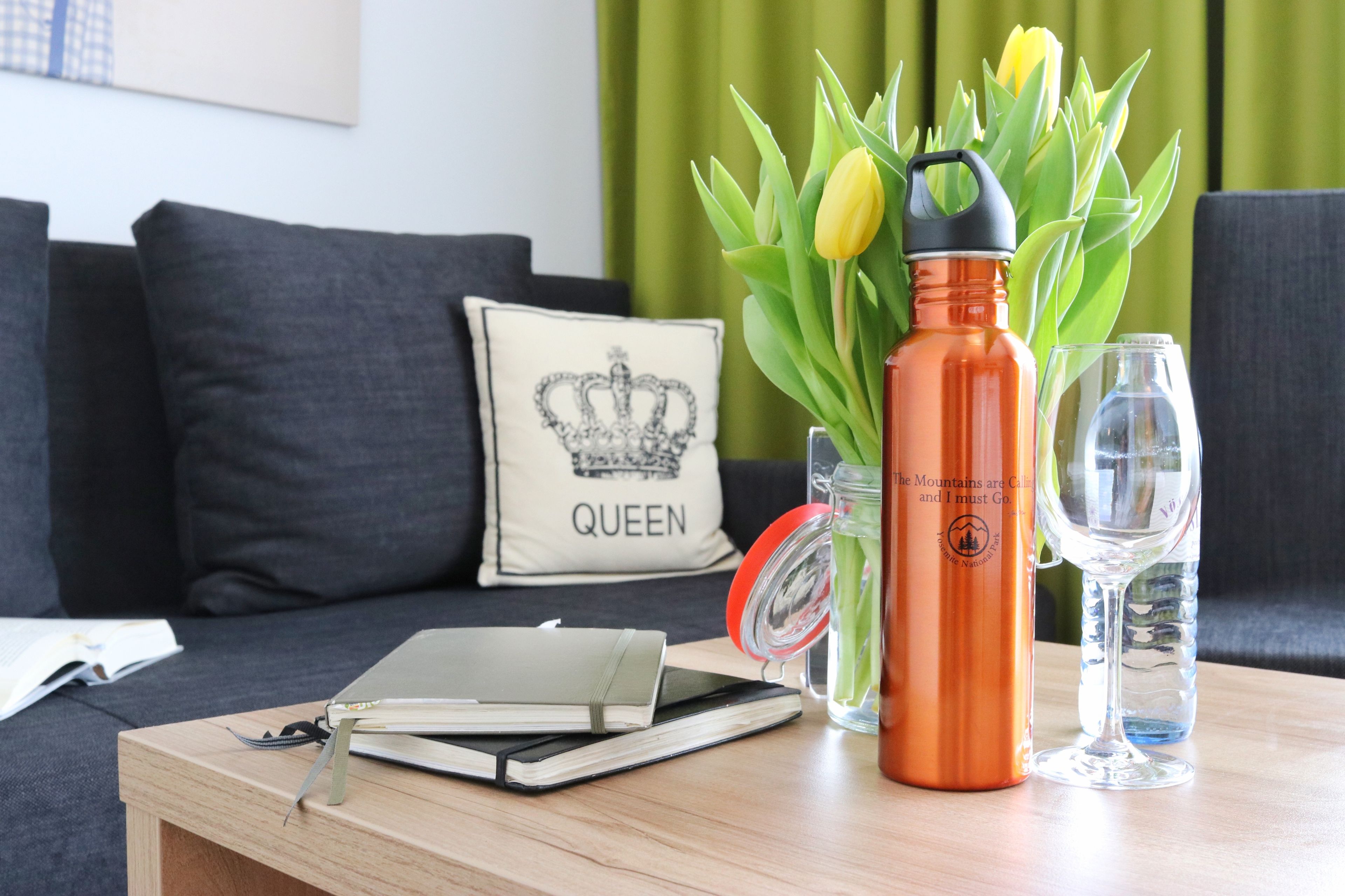 A wooden table with a notebook, a water bottle, a glass, and a vase with tulips.