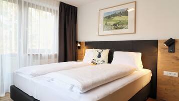 A neatly made bed with white linens, a headboard, and a wall-mounted lamp.