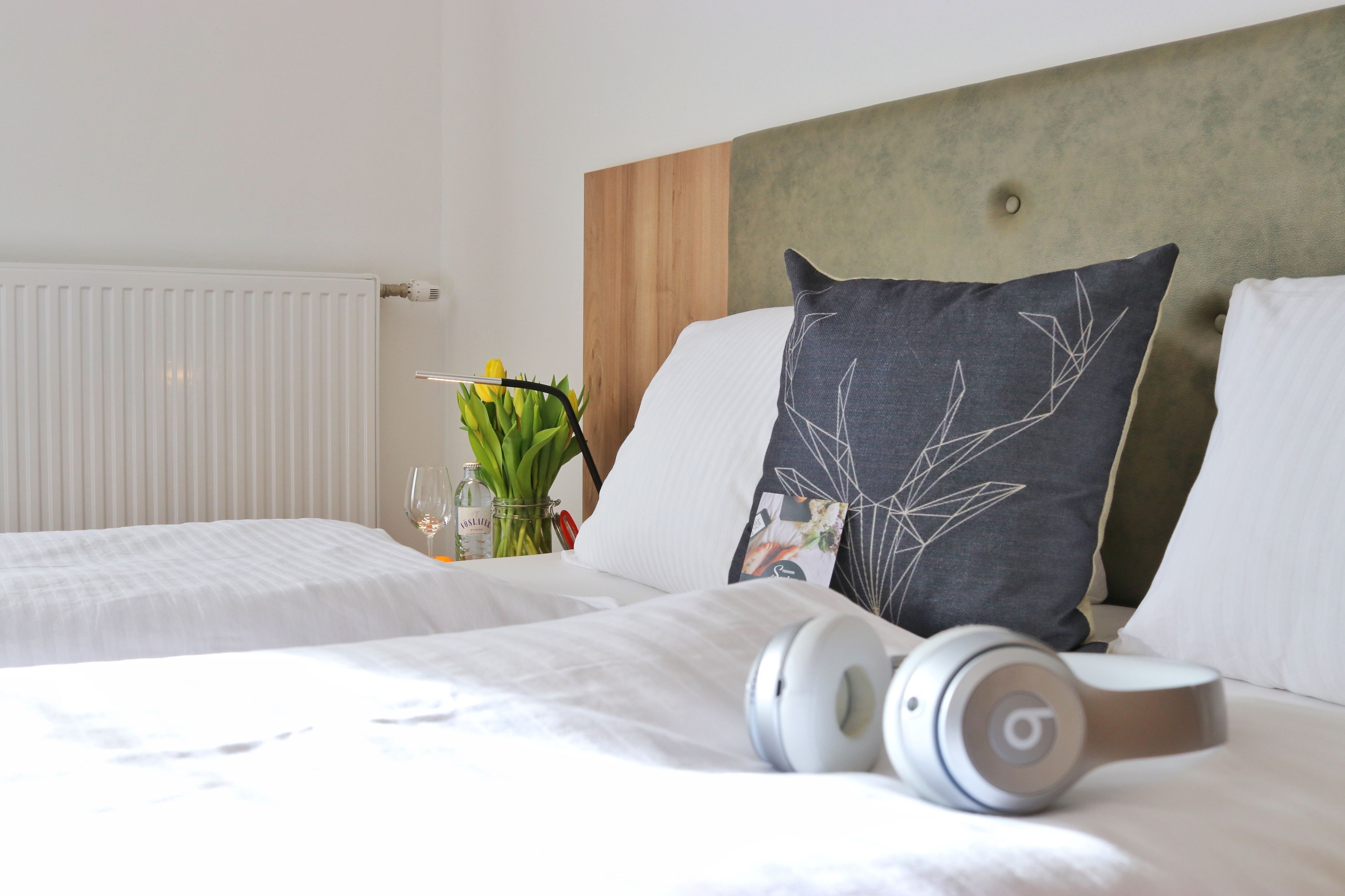 A hotel room with a bed, a headboard, and a pair of headphones on the bed.