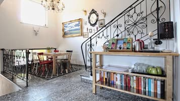 A dining area with a table and chairs, a bookshelf with books, a chandelier, and a staircase with a wrought iron railing.