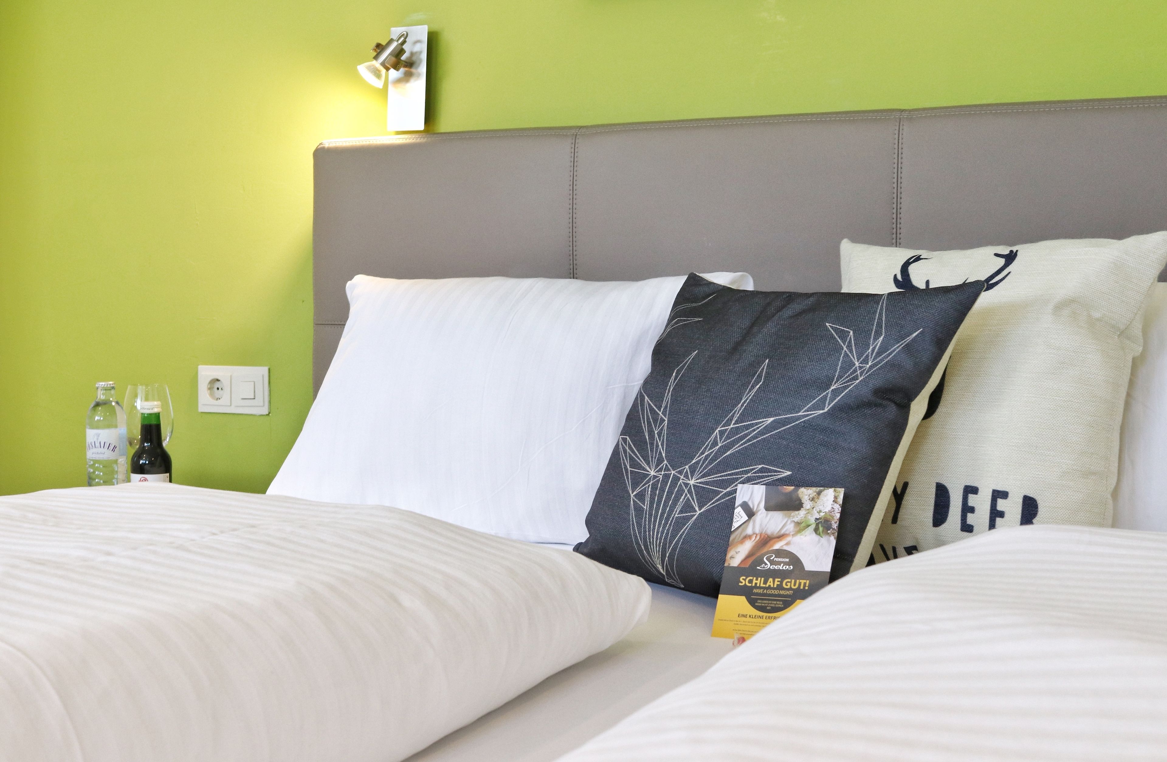 A neatly made bed with white linens, a grey headboard, and decorative pillows including one with a deer design.