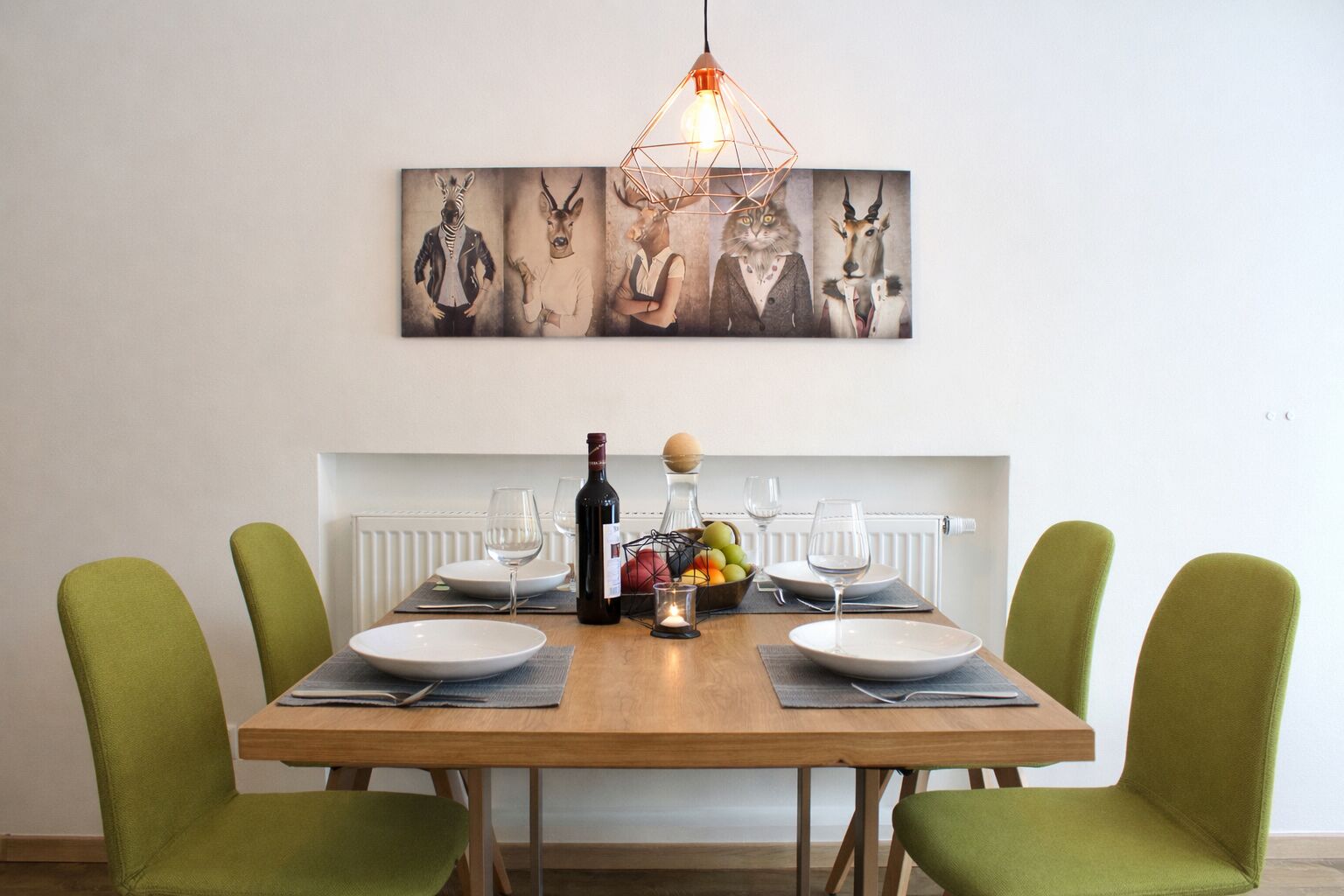 Una mesa de comedor con cuatro sillas, una botella de vino, copas y un frutero.