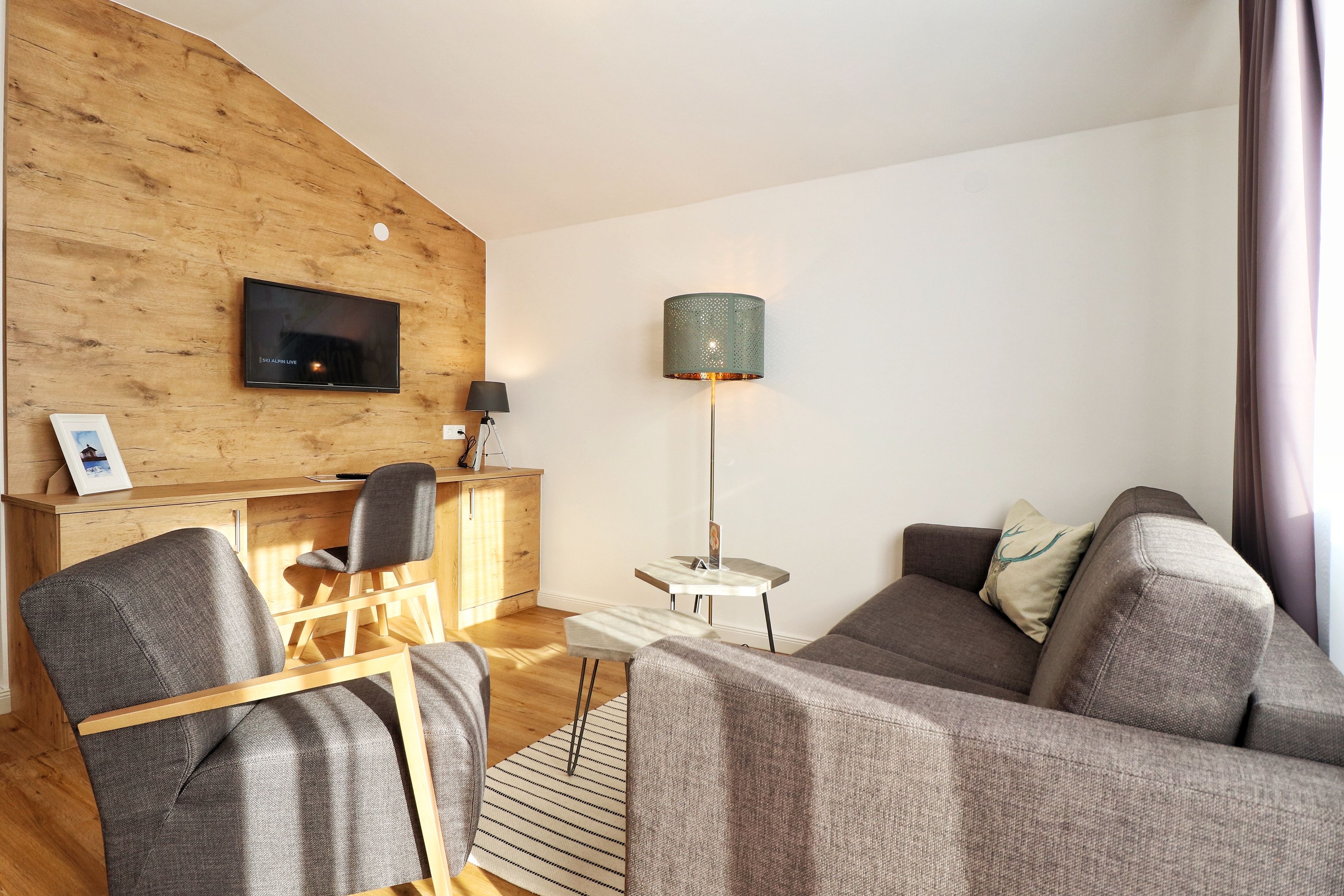 A modern living room with a wooden accent wall, a flat-screen TV, a lamp, a sofa, and a chair.