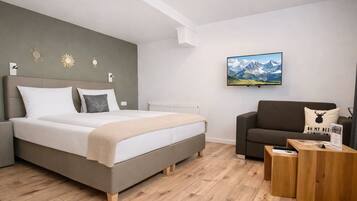A modern bedroom with a bed, a sofa, a coffee table, and a mountain landscape painting on the wall.