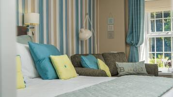 Un dormitorio con cama, sofá, papel tapiz a rayas, lámpara colgante y ventana con cortinas.