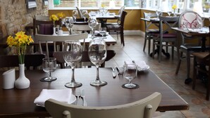 Un espace repas avec des tables mises pour le repas, comprenant des verres à vin et des couverts.