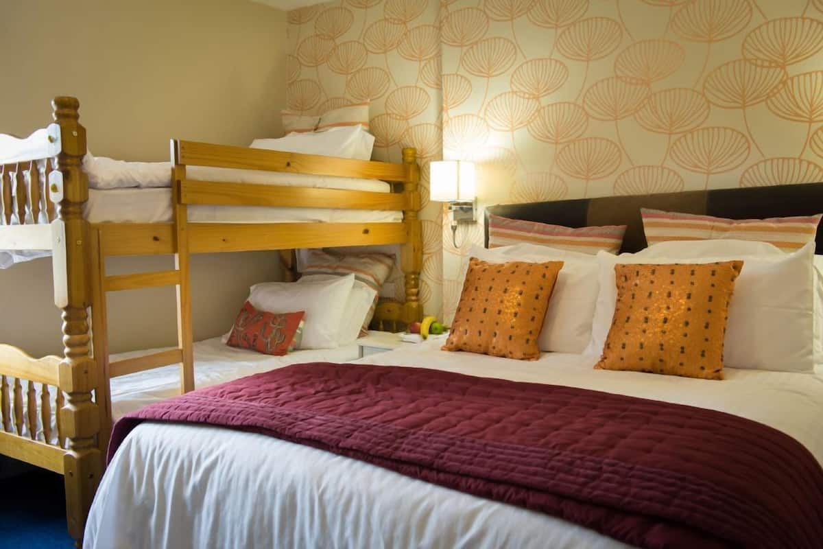 A room with a bunk bed, a single bed, and a nightstand with a lamp.
