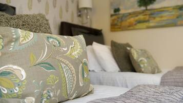 Una cama bien hecha con almohadones estampados, una lámpara de noche y un cuadro en la pared.