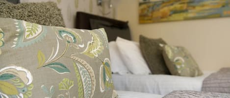 Una cama bien hecha con almohadones estampados, una lámpara de noche y un cuadro en la pared.