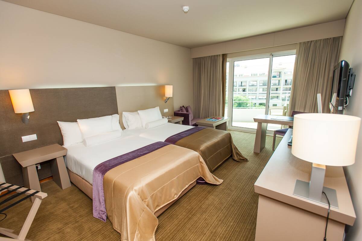 A hotel room with a large bed, a desk, a chair, a TV, and a view of the city through the window.