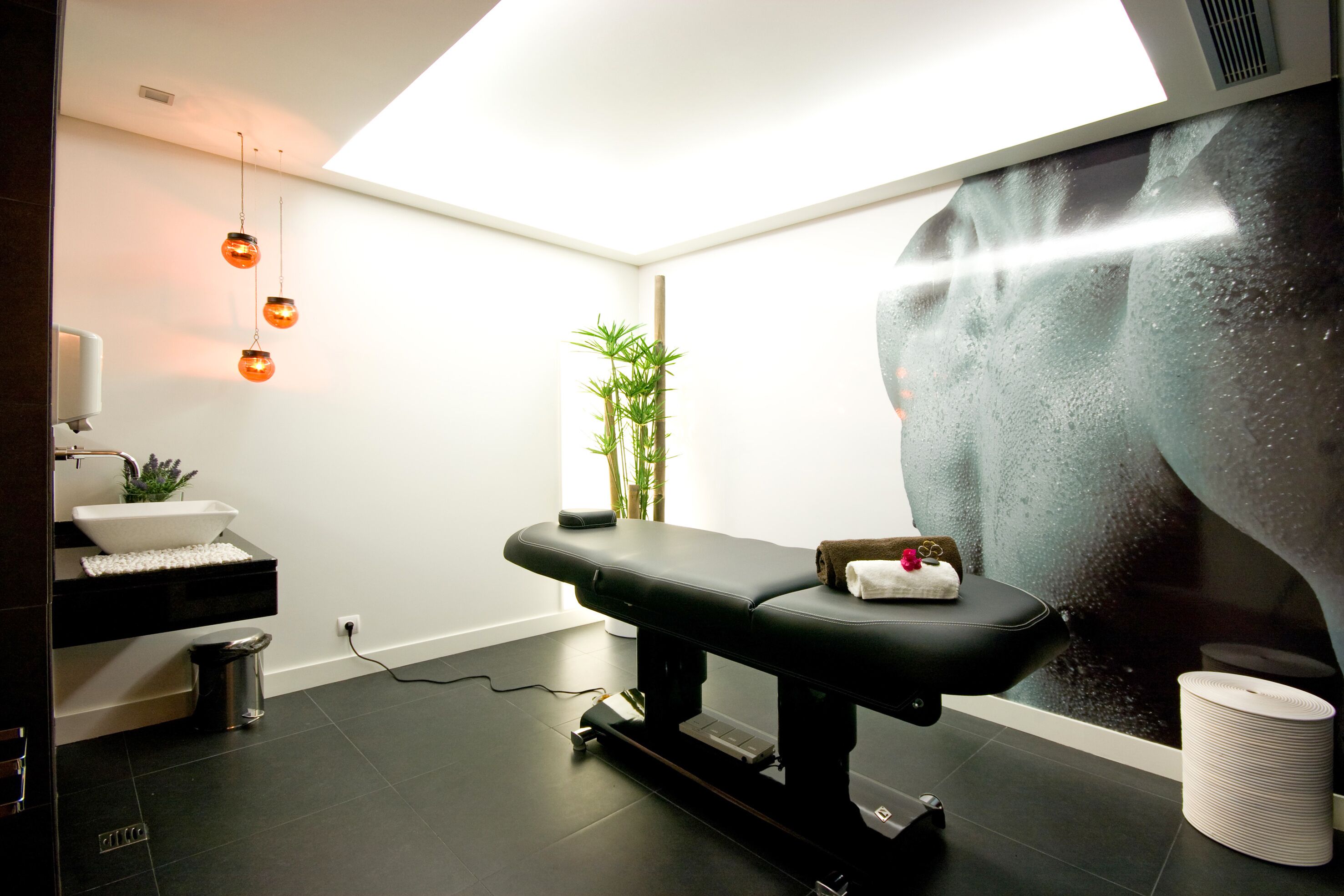 A modern spa room with a massage table, a small plant, and a large window with a view of a waterfall.