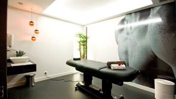 A modern spa room with a massage table, a small plant, and a large window with a view of a waterfall.