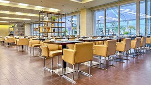 A spacious dining area with high tables and modern chairs, large windows, and a central shelving unit with decorative items. - Melia Madeira Mare (Funchal)