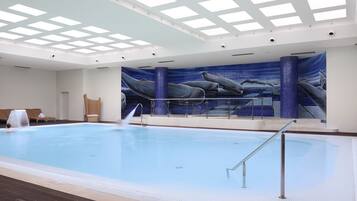 An indoor swimming pool with a mural of whales on the wall, a sunroof, and a lounge area with chairs.