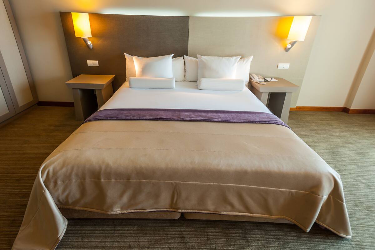 A hotel room with a large bed, two bedside tables, a nightstand, and two wall-mounted lamps.