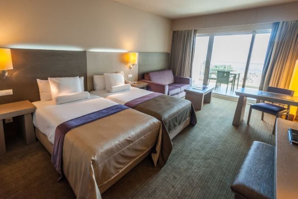 A hotel room with two beds, a desk, a chair, and a view of the beach.