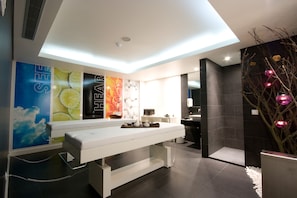 A modern spa room with a reception desk, a large poster wall, and a dark stone wall with a decorative plant.