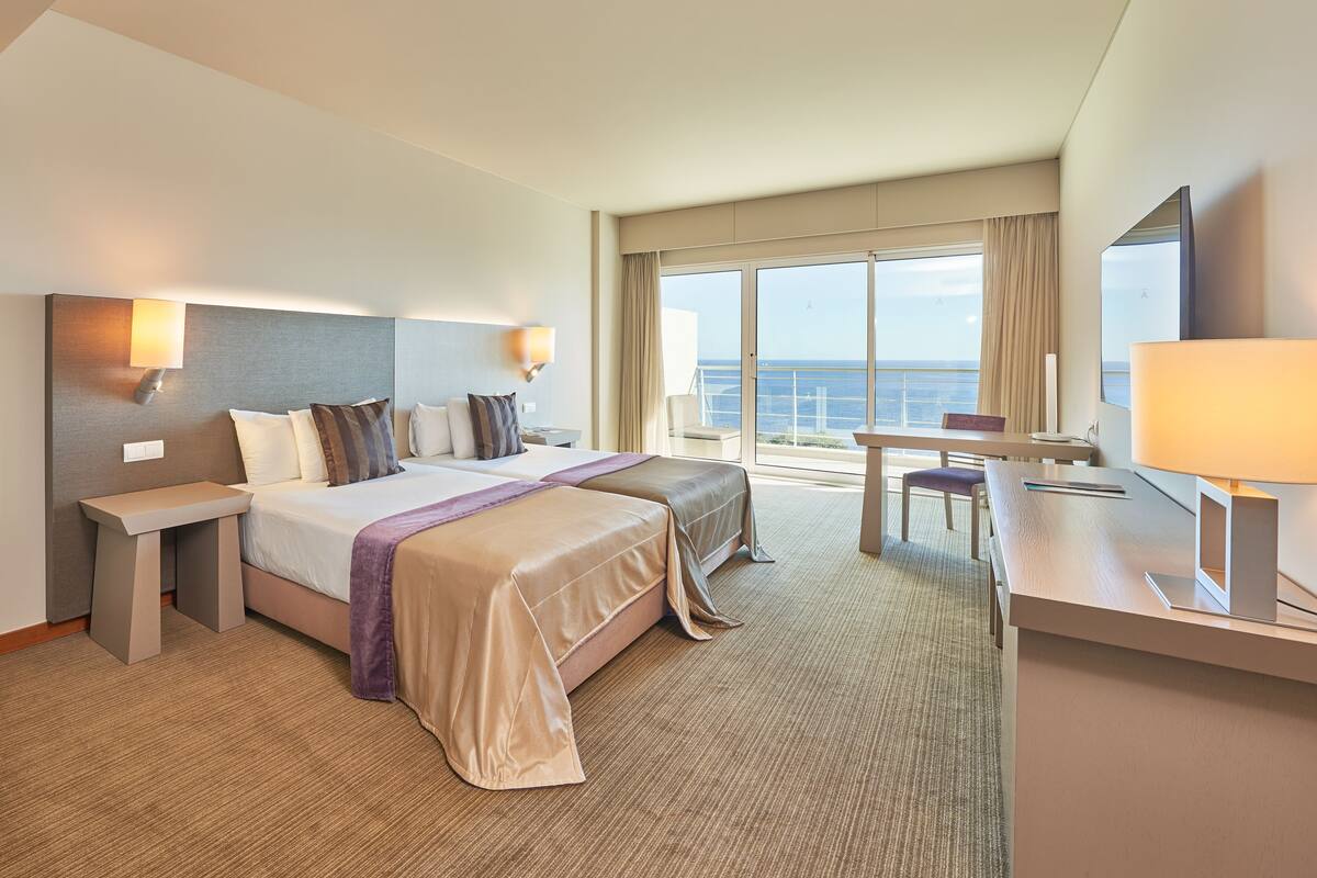 A hotel room with a large bed, a desk, a chair, and a view of the ocean.