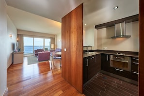 A modern kitchen with dark cabinetry and stainless steel appliances, a wooden floor, and a view of the sea through large windows.