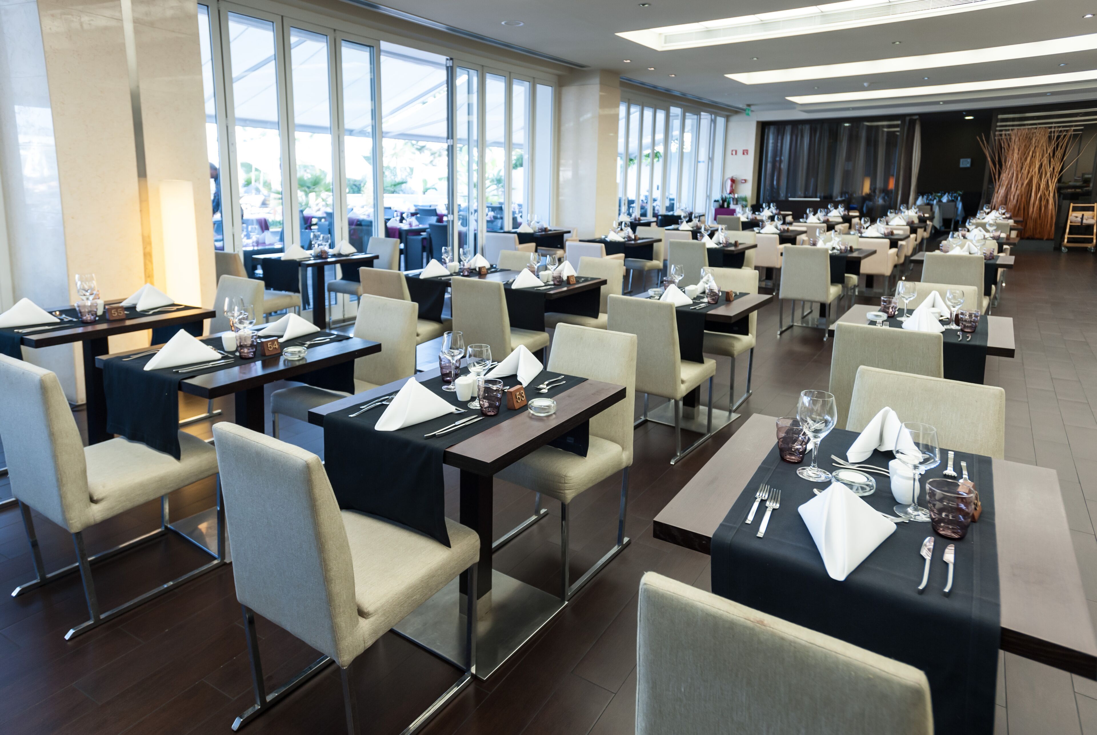 A spacious restaurant with multiple tables and chairs, large windows, and a modern interior design.