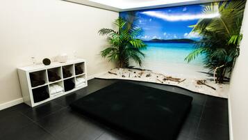 Quarto com carpete preto, estante branca com toalhas e um mural de praia na parede.