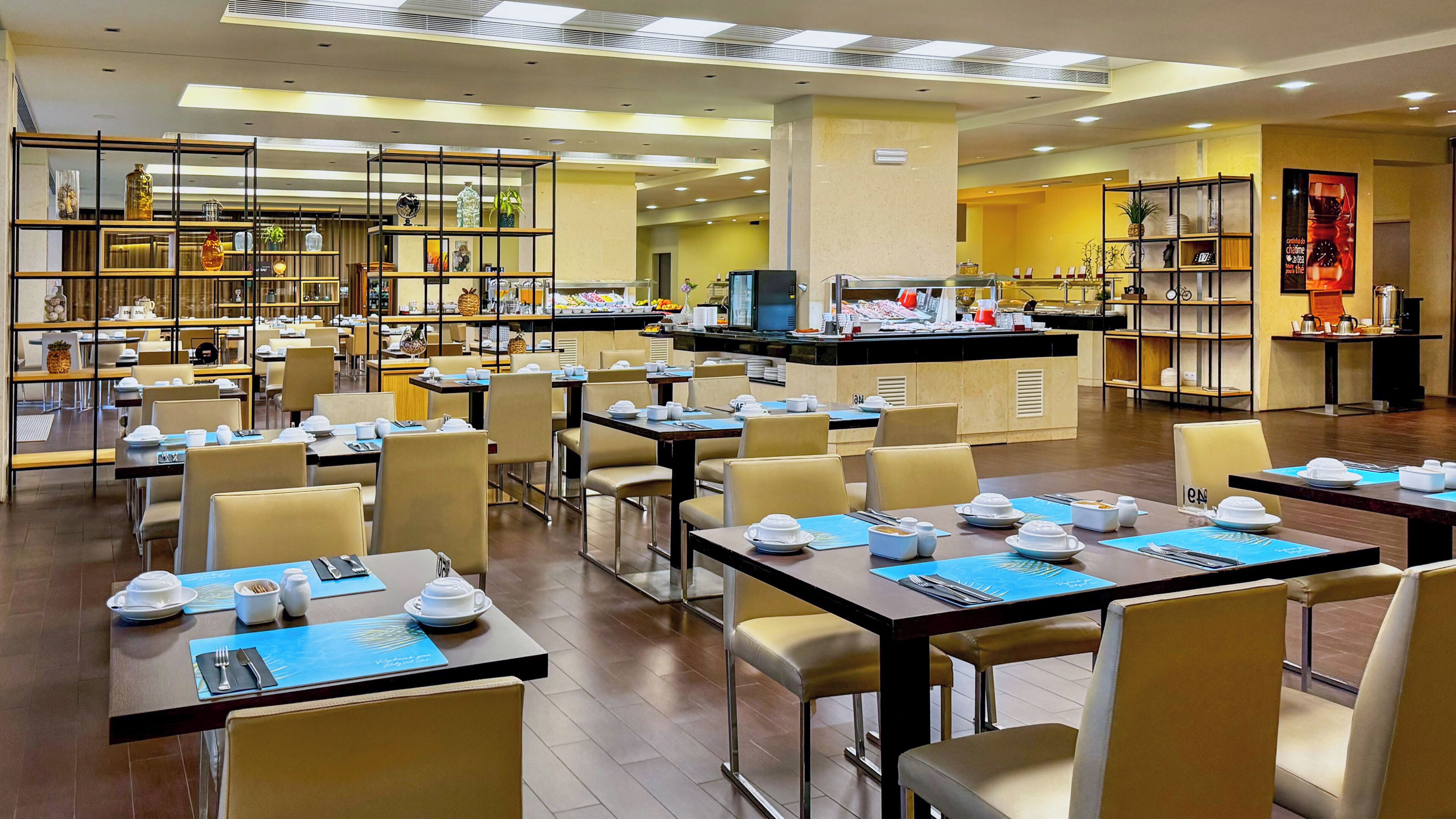 Un comedor de hotel con varias mesas y sillas, un mostrador de buffet y diversos objetos decorativos en estantes.