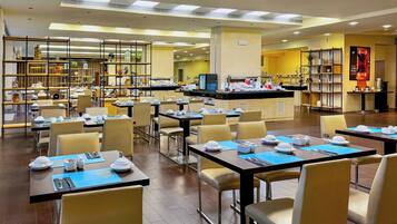 Un comedor de hotel con varias mesas y sillas, un mostrador de buffet y diversos objetos decorativos en estantes.