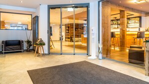 Un moderno vestíbulo de hotel con una zona de recepción, un espacio de descanso y un bar.