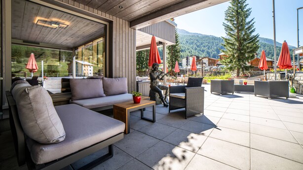 Un área de estar al aire libre con sofá, sillas y una mesa, con vistas a un paisaje montañoso.