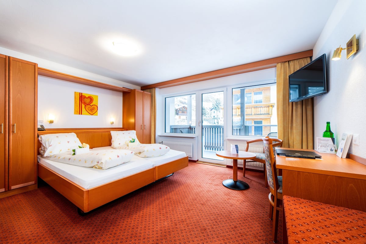 A hotel room with a bed, a desk, a chair, a TV, and a window with a view of buildings.