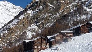 Una cabaña de montaña con cabañas de madera, techos cubiertos de nieve y un telón de fondo de montañas escarpadas.