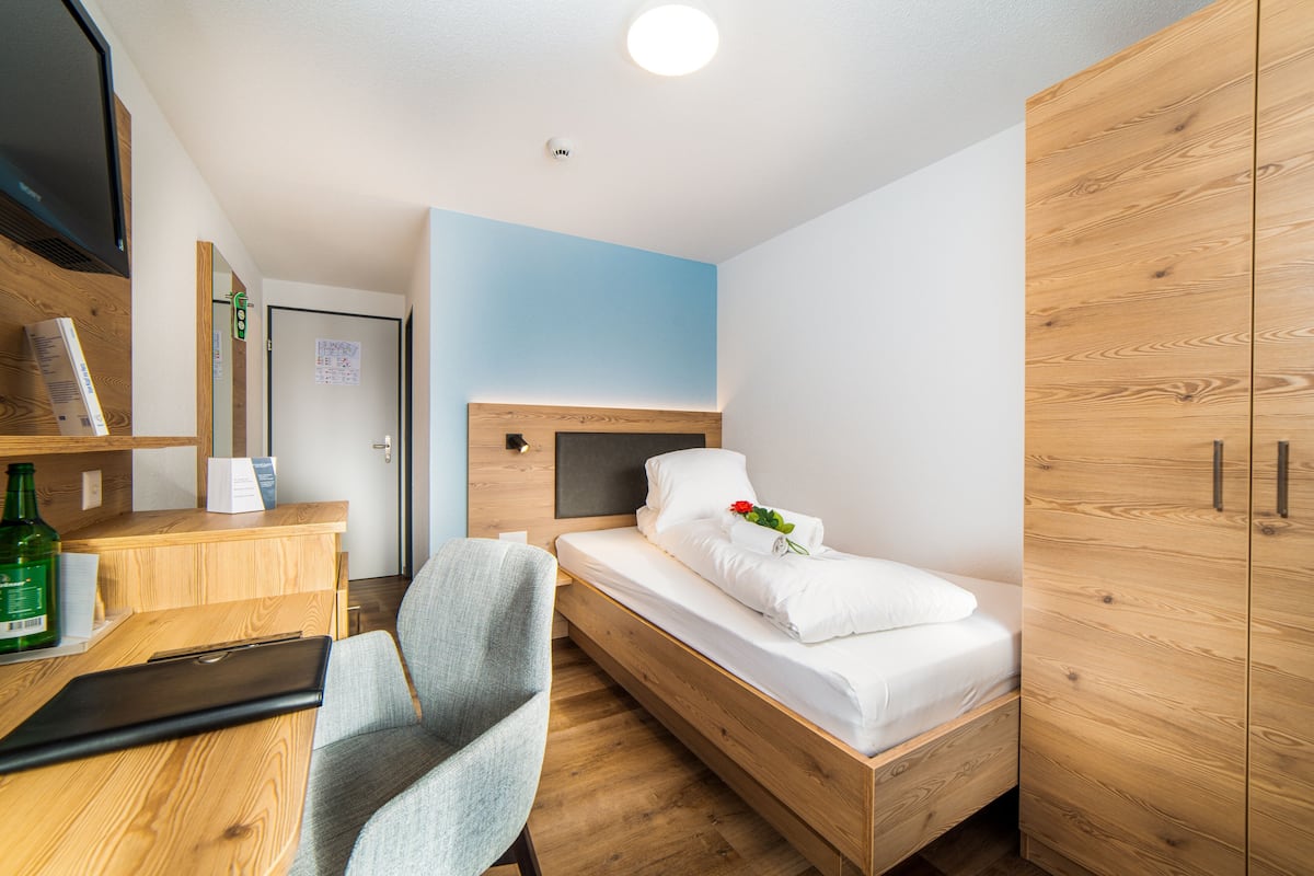 A compact room with a bed, a desk, a chair, and wooden wardrobe.