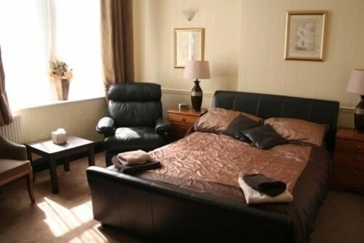 A hotel room with a bed, a chair, a small table, and a lamp.