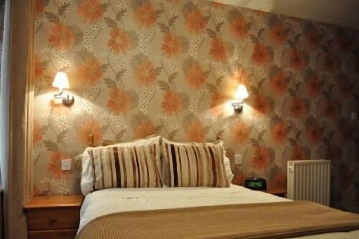 A bedroom with a floral wallpaper, a bed with striped bedding, two bedside lamps, and a radiator.